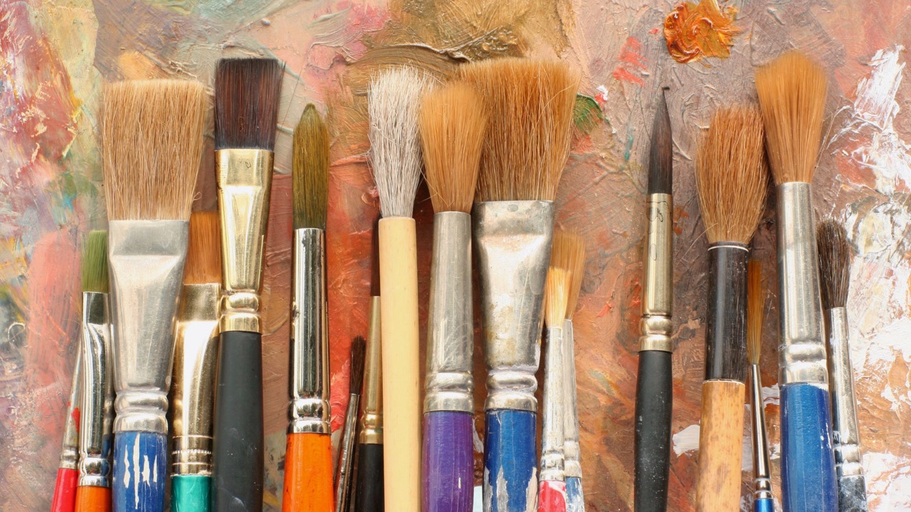 Verschiedene Malpinsel auf farbiger Leinwand